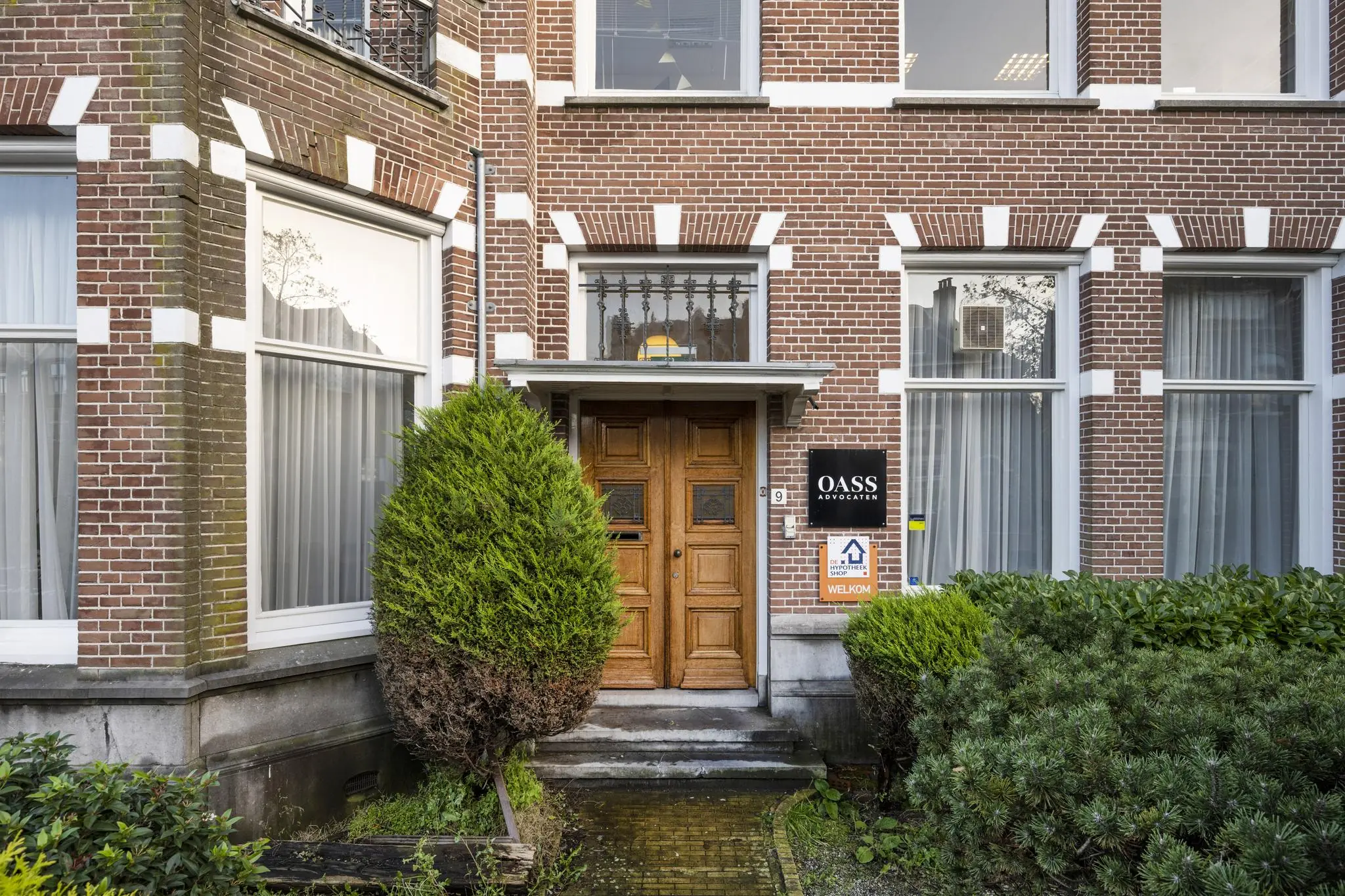 Voorgevel van het kantoorpand van OASS Advocaten aan de Van Eedenstraat met houten voordeur en omliggend groen.